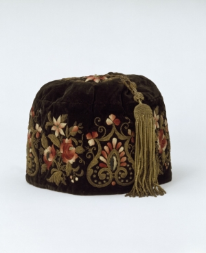 A smoking cap from the 1860's, made in South America for the Portuguese market. It is made from embroidered velvet and lined with silk, the long tassel is also of silk