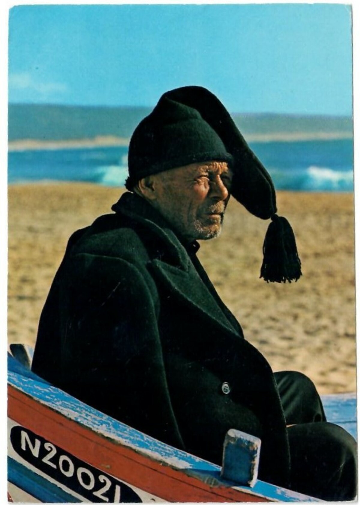 Portuguese postcard from the mid-20th century, showing an elderly fisherman wearing a long black cap with tassel (TRC 2020.0004).