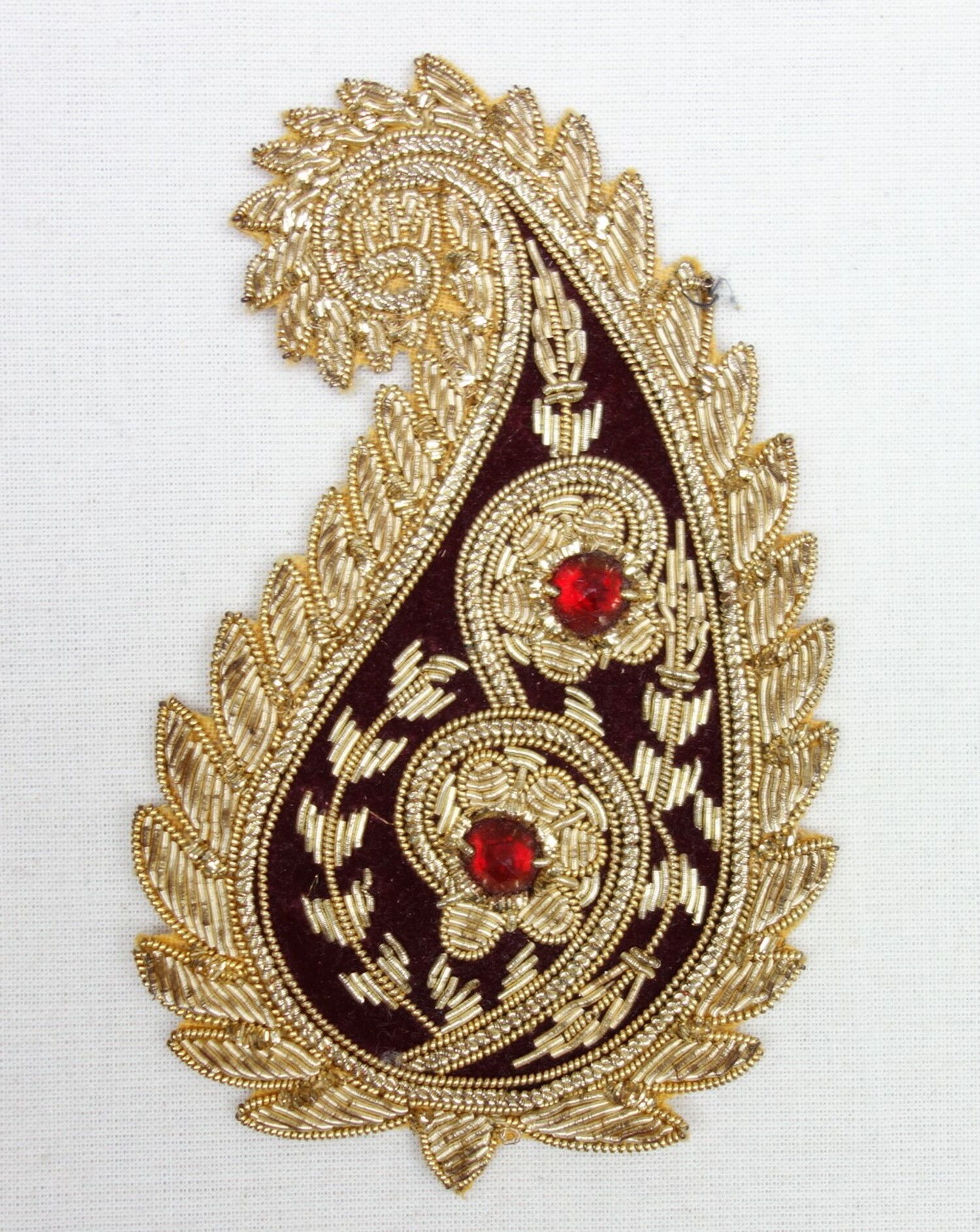 Indian appliqué in the shape of an ornate paisley/buteh motif, hand embroidered in gold thread on a dark red velvet ground. Mid-20th century (TRC 2020.5154).