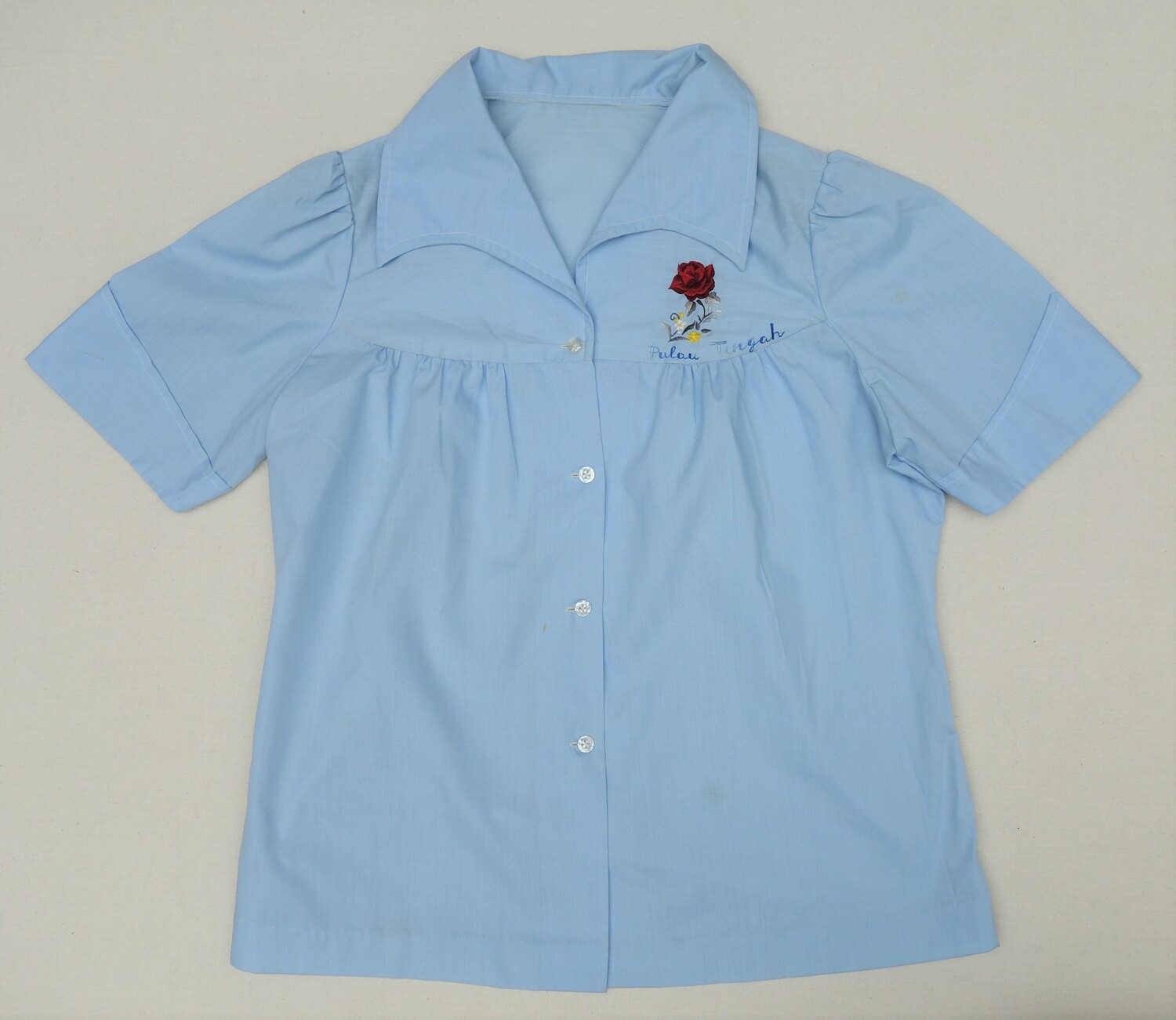 Child's blouse with embroidered bunch of flowers and the name of the island and camp of Pulau Tengah, Malaysia, specially set up for Vietnamese boat people in 1975 (TRC 2021.0417).
