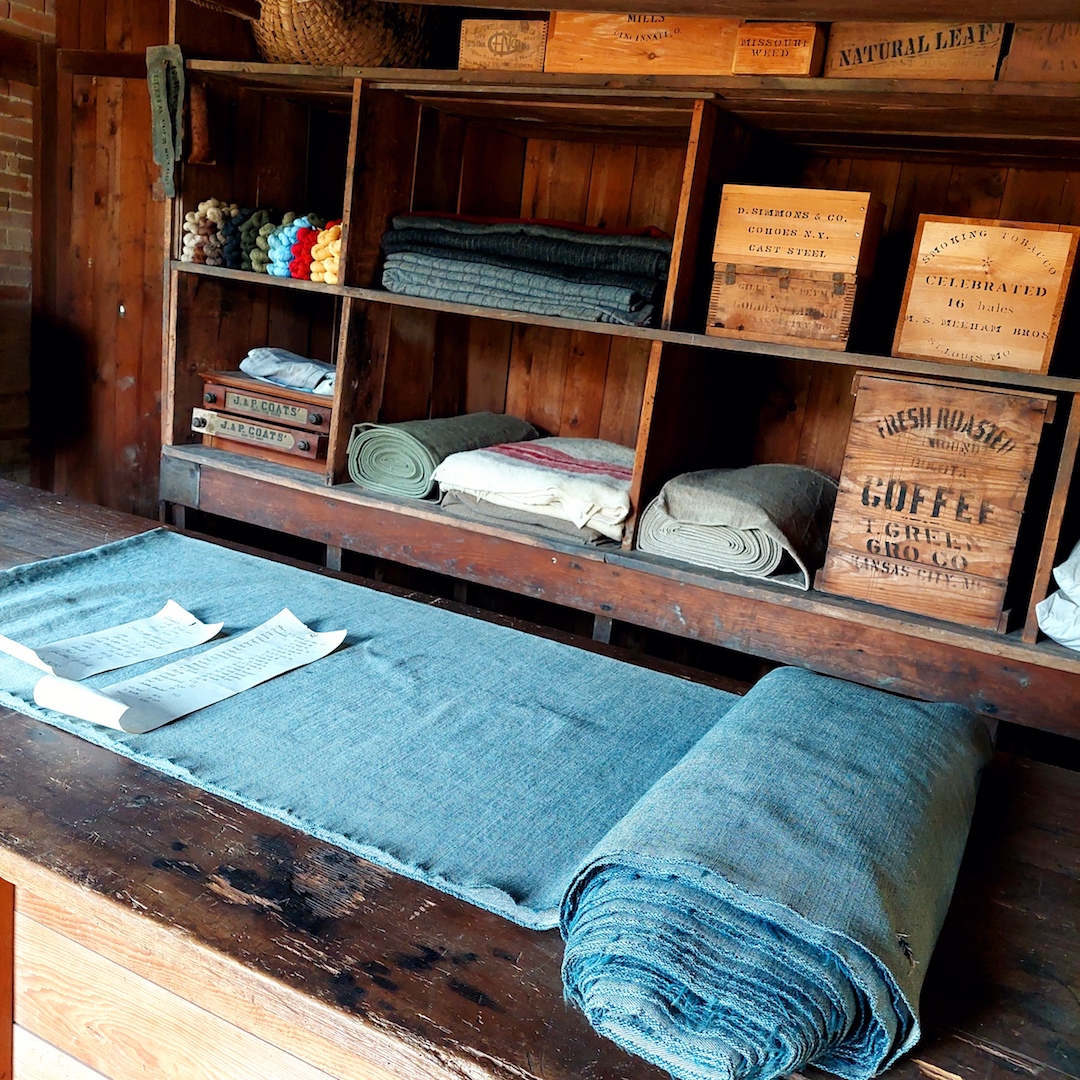 The store attached to the Mill, and a bolt of Mill-produced cloth. A pair of wool blankets cost $6.00 in 1877; a ‘fancy’ (or patterned) pair cost $9, while a pound of 3-ply yarn cost between 65 to 75 cents. Photo by Shelley Anderson.