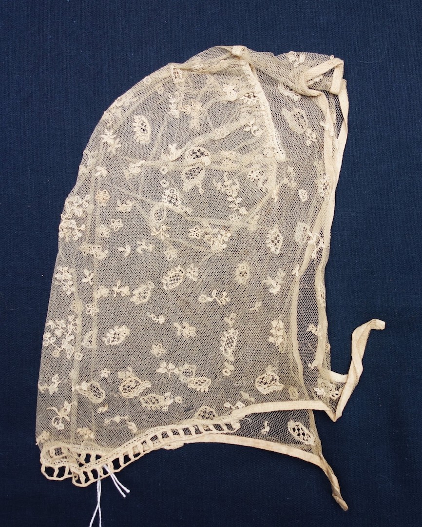 Lace cap made from a very fine net (tulle) with applied embroidered and appliqué motifs of various types and sizes. The Netherlands, 19th century (TRC 2024.1174).