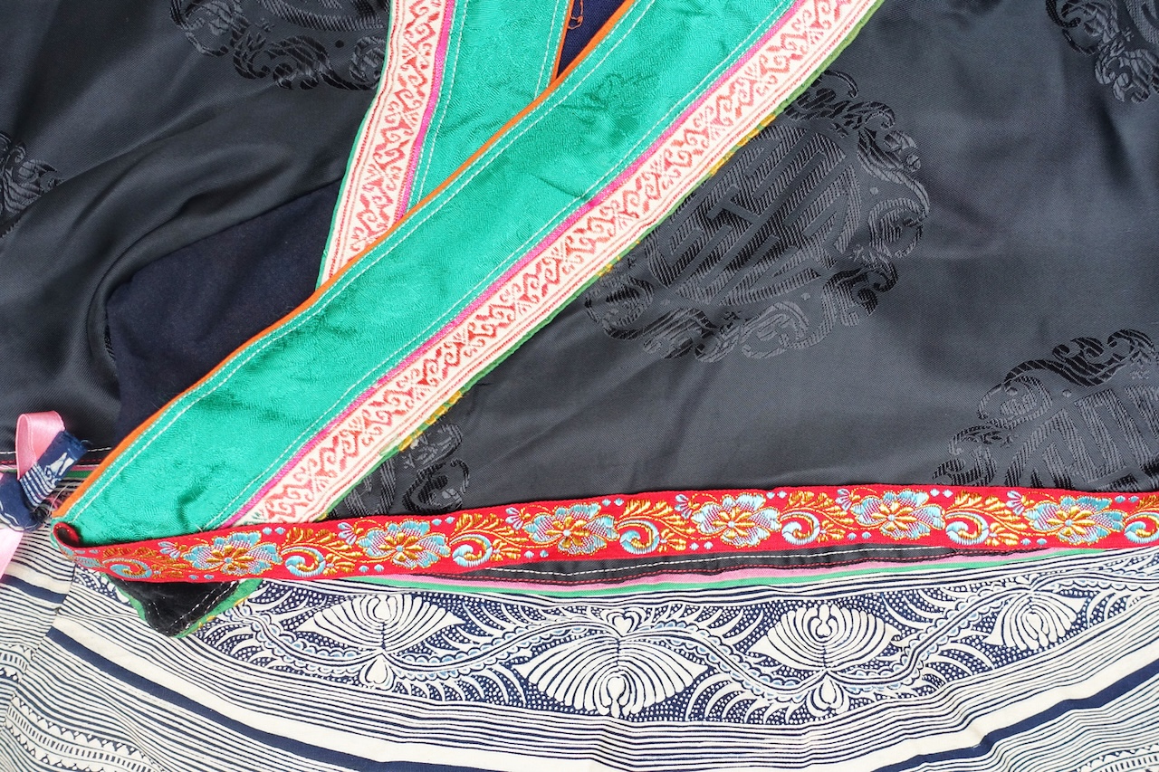 Fig. 12. Detail of the jacket showing the black damask fabric with woven Chinese characters, together with batik motifs and decorative woven bands. Douqing Miao, East Guizhou, China, 20th century (TRC 2024.2867).