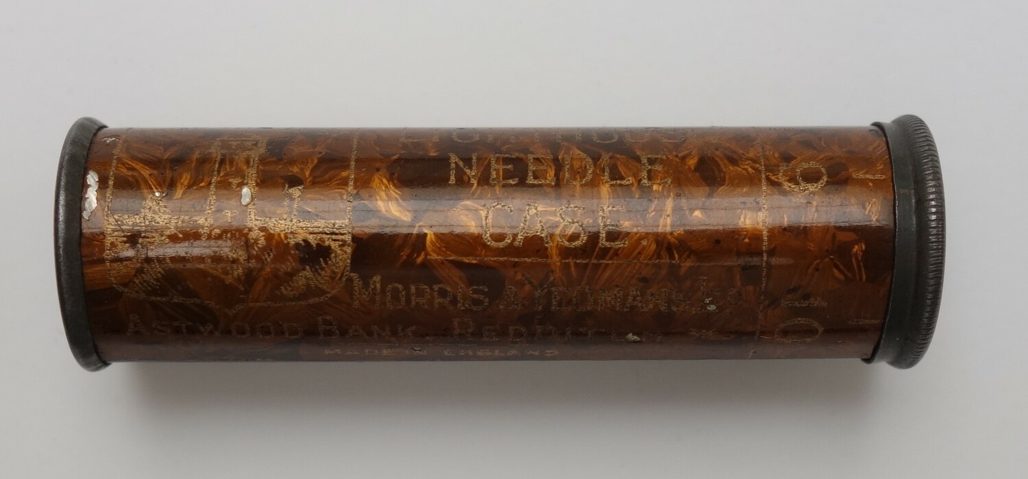 Round orange and brown metal case containing needles. The packaging has the text "THE LIGHTHOUSE NEEDLE CASE." UK, 1890-1900 (TRC 2025.0674).