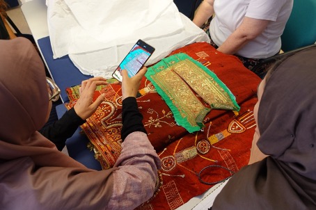 A participant photographs a green front piece of a dress (TRC 2011.0036) on top of a red shawl from Tunisia (early 20th century) (TRC 2018.0276). Photograph by Christina de Korte.