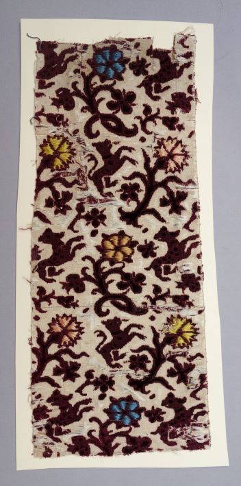 Sample of mid-17th century voided and ciselé velvet  with a design of dogs in a colourful forest (TRC 2011.0385).