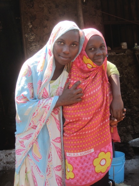 Two women from Zanzibar wearing a kanga. The woman to the right has a kanga with the text "Alaa kumbe", which means something like 'Good gracious me!'. Photograph by Kate Kingsford.